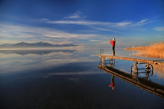 Fotografin steht am Ende des Stegs vom Chiemsee und fotografiert in die Chiemgauer Alpen