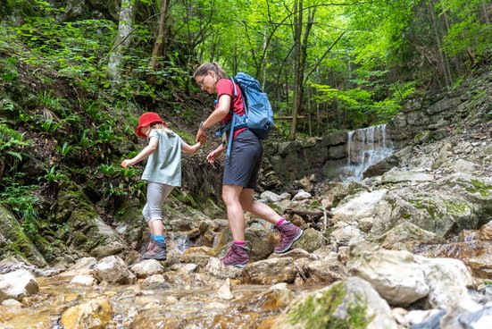 Mutter und Tochter überqueren kleinen Bach beim Wandern im Wald 