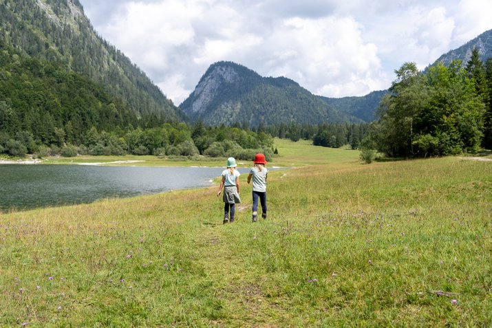 Geschwister spielen auf der Wiese vor See und Berge 